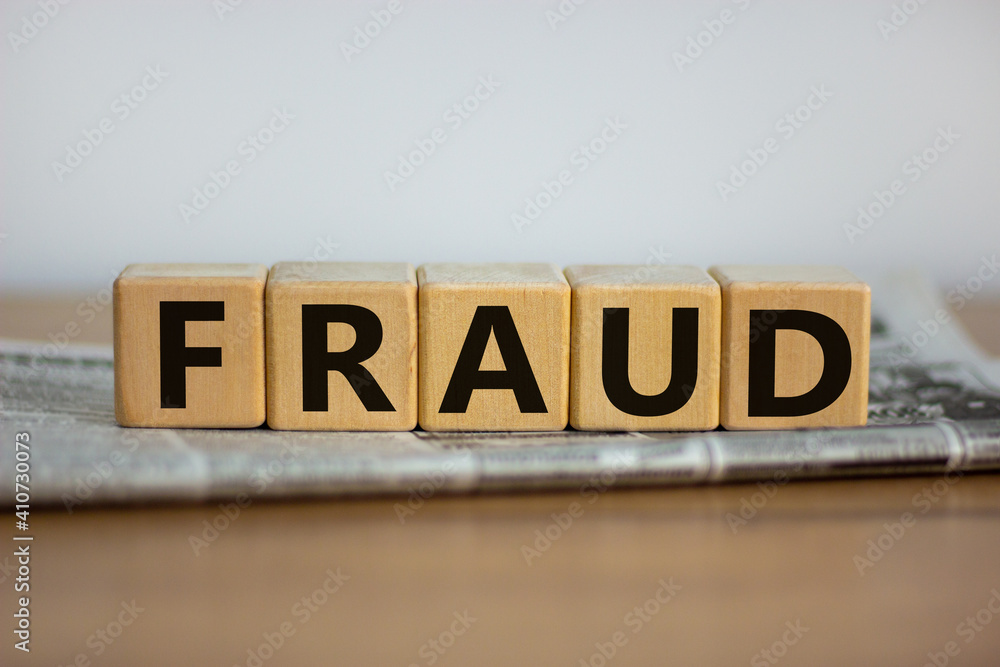 Fraud symbol. Wooden cubes placed on a newspaper. The word 'fraud'. Beautiful wooden table. White background. Business and fraud concept. Copy space.