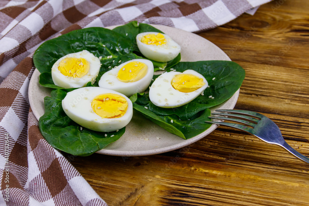 Boiled eggs with fresh spinach leaves and sesame seeds on wooden table