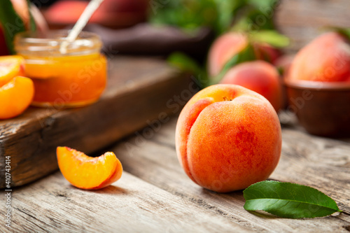 Peach fruit with leaf. Ripe juicy orange peach fruit on wooden table. Peach harvest and jam on rustic kitchen closeup in dark mood. Whole peach fruit and wedges for making jam