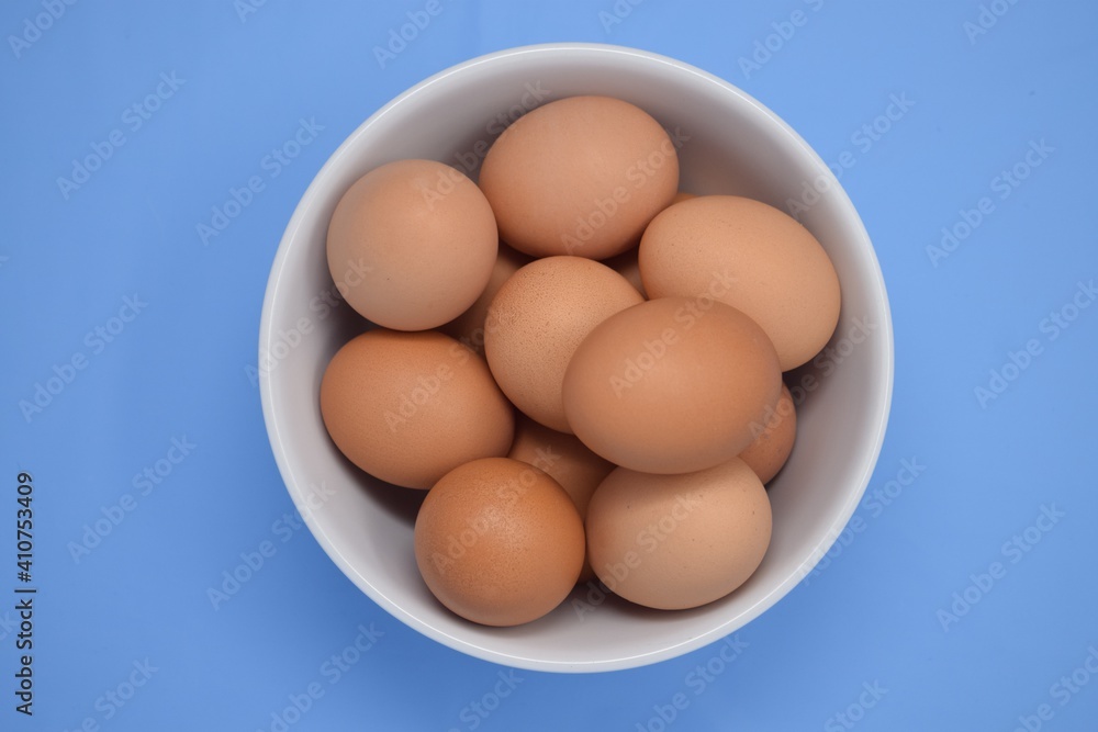 Overhead bowl of farm fresh eggs in a white ceramic bowl on an eggshell blue background Overhead bowl of farm fresh eggs in a white ceramic bowl on an eggshell blue background