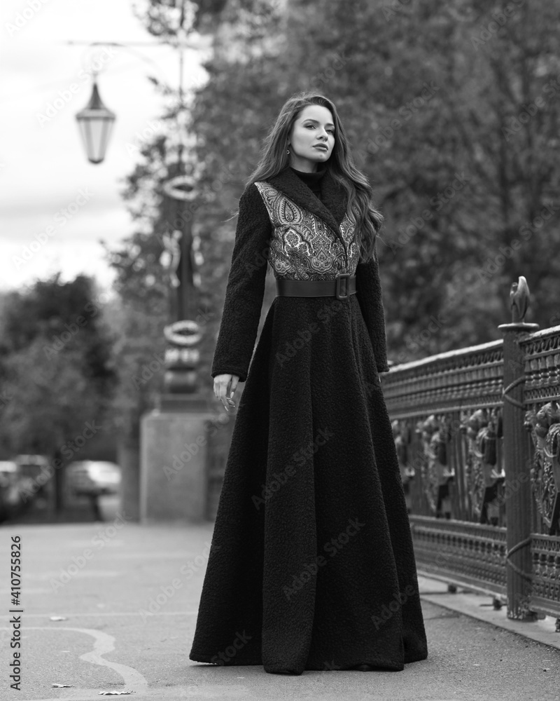 Elegant woman wearing blue coat and walking city street on autumn or fall day against town park fence. Pretty girl with makeup and wavy brunette hair Elegant woman wearing blue coat and walking city street on autumn or fall day against town park fence. Pretty girl with makeup and wavy brunette hair
