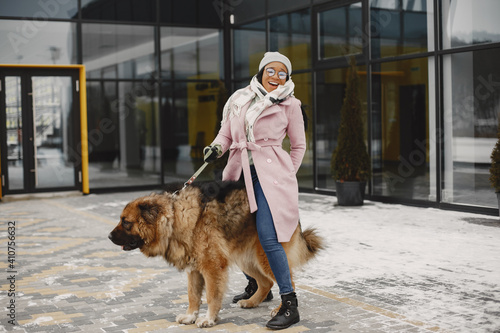 Cute african girl in a winter park. Woman in a pink coat. Lady with a dog.