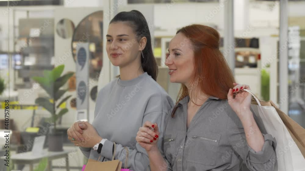 Female friends examining items on sale in the showcase at the mall. Two cheerful young women enjoying shopping together, looking at the display of a store Female friends examining items on sale in the showcase at the mall. Two cheerful young women enjoying shopping together, looking at the display of a store