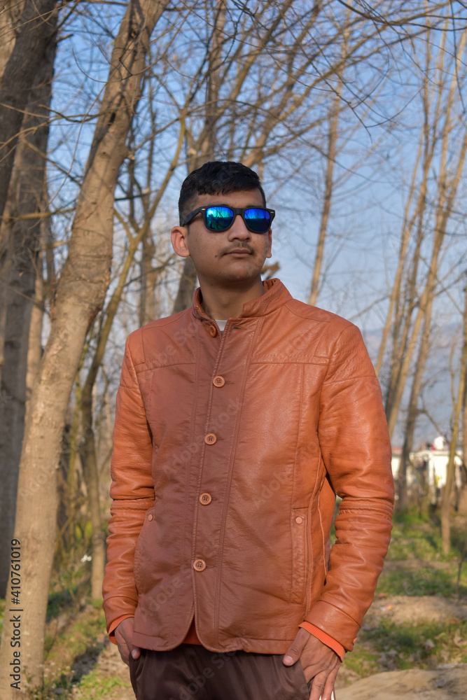 outdoor portrait of indian ethnicity boy looking sideways wearing blue sunglasses and brown leather coat outdoor portrait of indian ethnicity boy looking sideways wearing blue sunglasses and brown leather coat