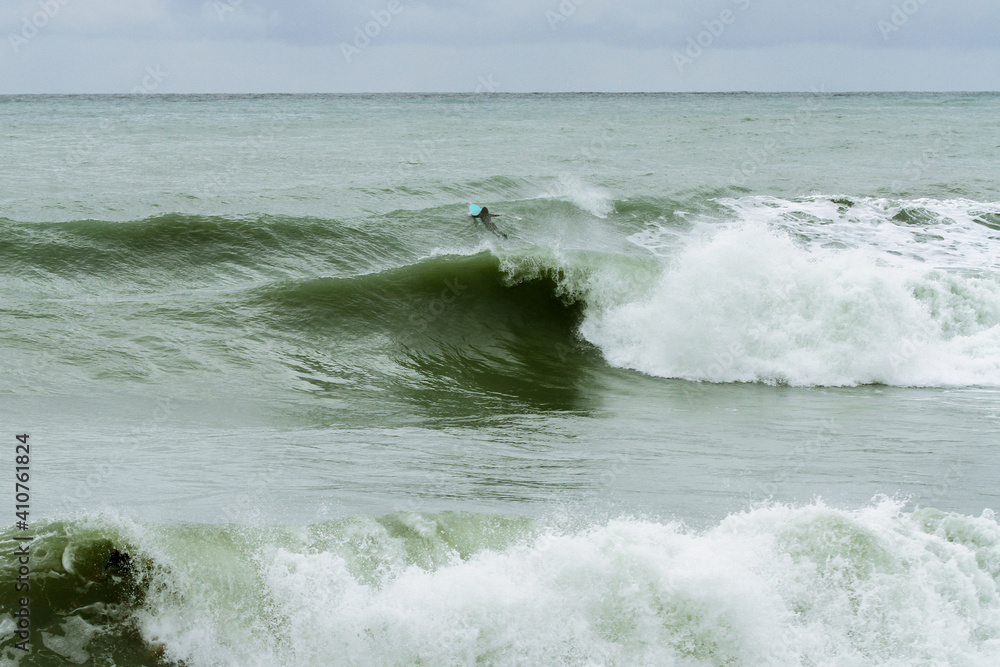 Fototapeta premium Surfer girl alone swims big green waves in the cold sea