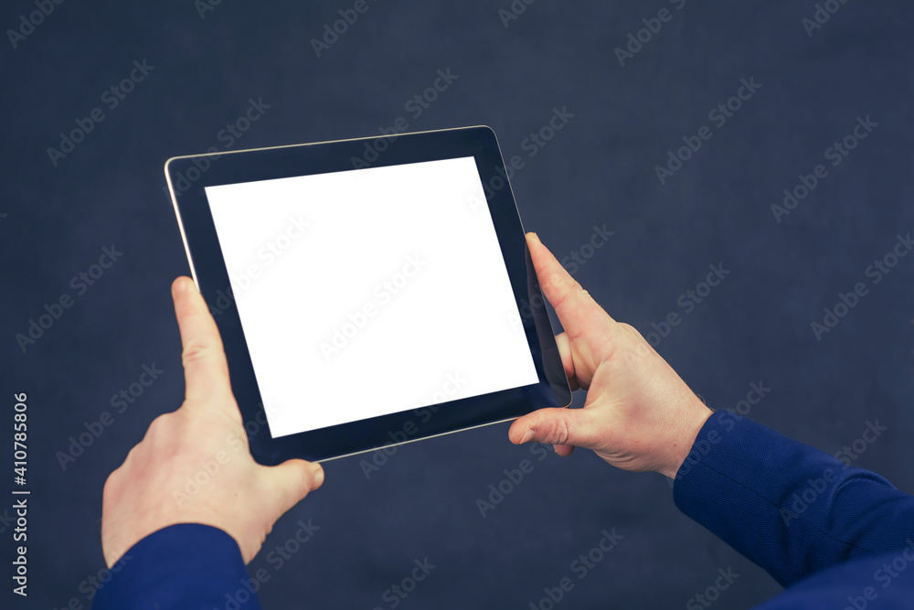 Businessman in a blue jacket holds a mock-up of a tablet with a white screen on a dark background. Businessman in a blue jacket holds a mock-up of a tablet with a white screen on a dark background.