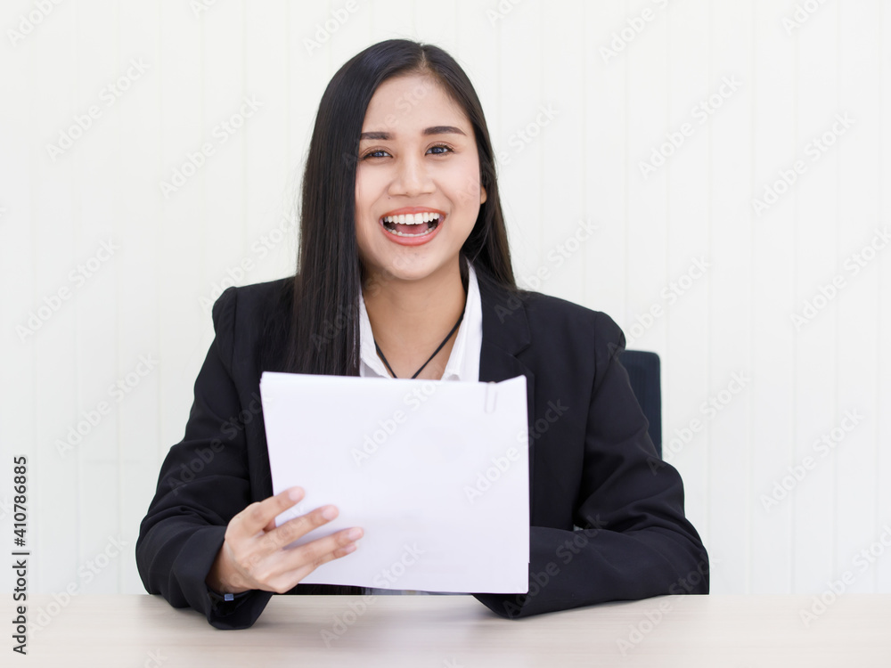 portrait of young beautiful and happy Asian woman wearing smart casual laughing with friendly and cheerful face holding paper sitting on a desk celebrate for her success portrait of young beautiful and happy Asian woman wearing smart casual laughing with friendly and cheerful face holding paper sitting on a desk celebrate for her success