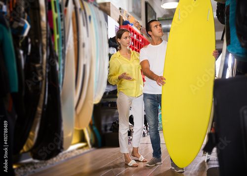 Photography Young glad couple choosing surfboard in sporting goods store