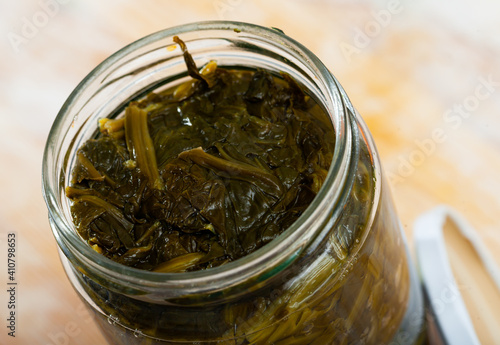 Canned green spinach in opened glass jar on wooden surface, nobody