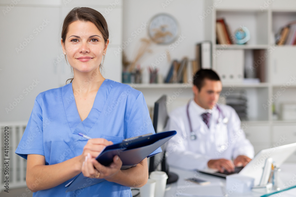 Fototapeta premium Polite female doctor meeting patients in medical office, filling out medical form on clipboard