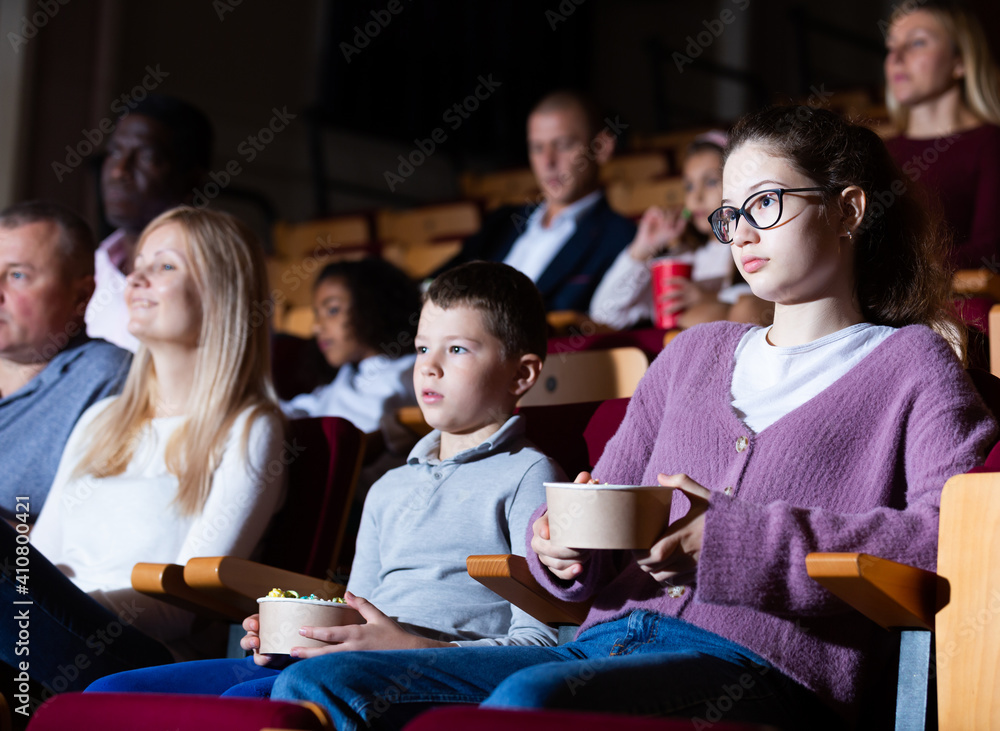 Obraz premium Portrait of teen girl with family sitting in movie theater with popcorn and drinks, watching interesting film