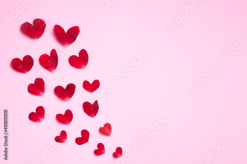 Pink background with rose petals in the shape of a heart, with rose, white candles and paper.
