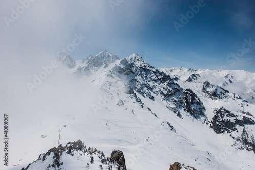 View of mountain peaks and rocks covered with snow around the clouds under the blue sky