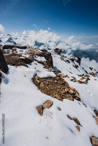 View of mountain peaks and rocks covered with snow around the clouds under the blue sky