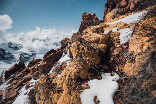 View of mountain peaks and rocks covered with snow around the clouds under the blue sky