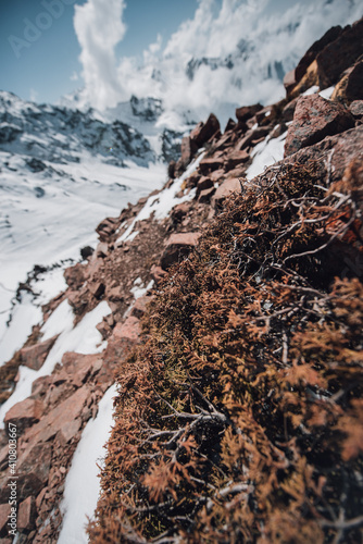 View of mountain peaks and rocks covered with snow around the clouds under the blue sky