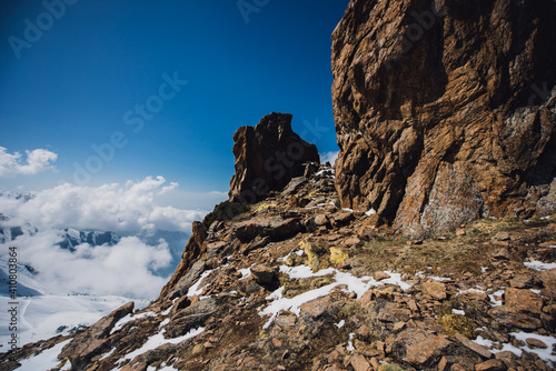 View of mountain peaks and rocks covered with snow around the clouds under the blue sky