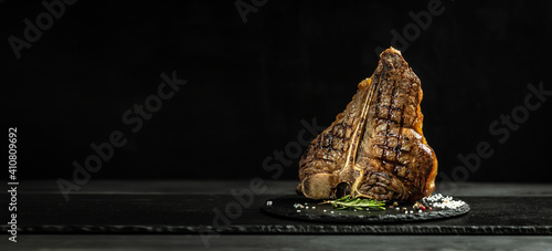 Piece of cooked T-bone or aged wagyu porterhouse grilled beef steak with spices served on on stone board. Long banner format, top view
