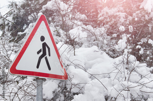 Pedestrian sign in red triangle and trees bushes covered with heavy snow.