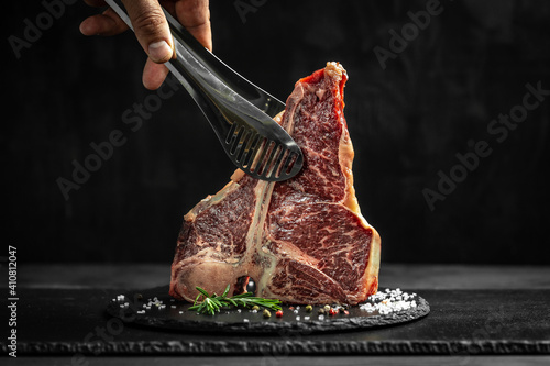 Cooking meat by chef hands raw porterhouse steak, dry-aged with herbs, pepper and salt. menu restaurant or recipe text photo