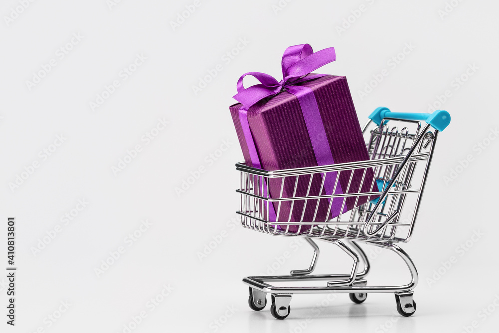Shopping cart (toy) with gifts in large box, packed in purple paper. Copy space. Discounts, sale. Shopping cart (toy) with gifts in large box, packed in purple paper. Copy space. Discounts, sale.