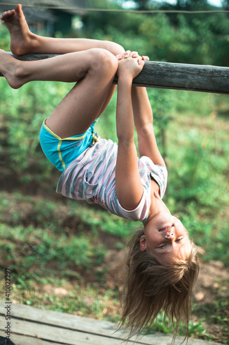 Obraz na plátne Little girl hanging upside down on green rural countryside.