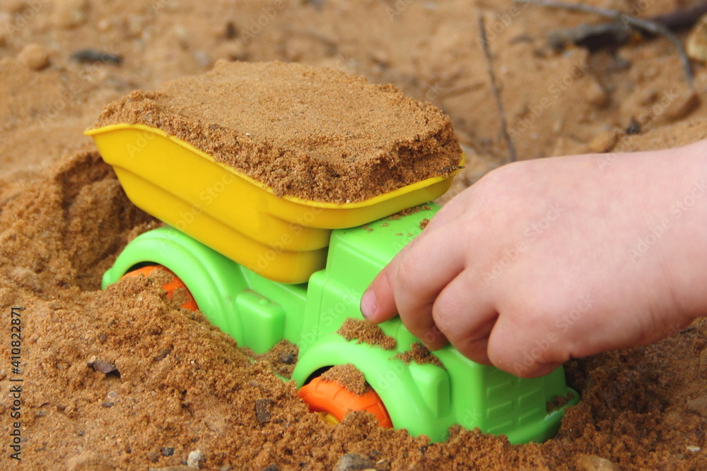 Bright colorful yellow green plastic toy tipper truck in kid hand close up loaded sand truck toy in outdoor sandbox Bright colorful yellow green plastic toy tipper truck in kid hand close up loaded sand truck toy in outdoor sandbox