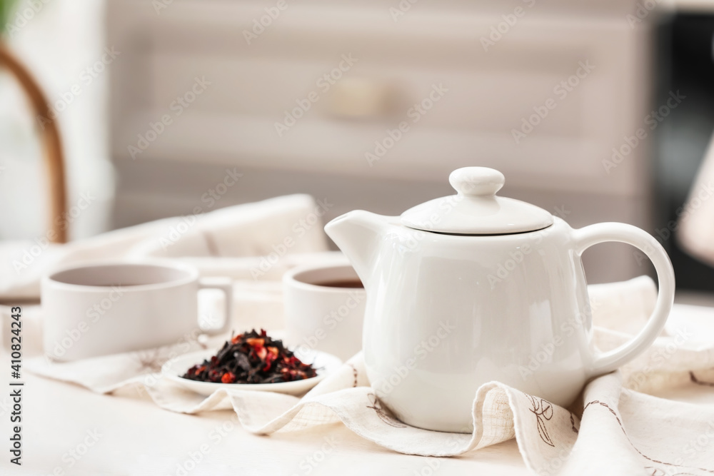 Teapot and dry tea leaves on light table in room Teapot and dry tea leaves on light table in room