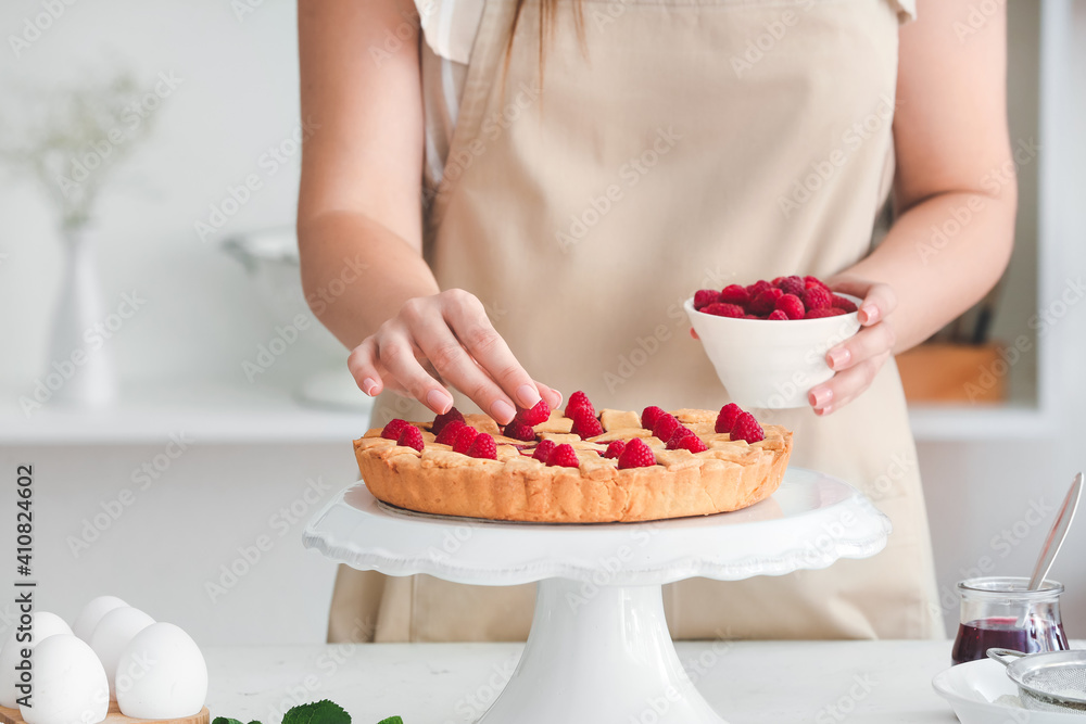 Woman decorating tasty raspberry pie in kitchen, closeup