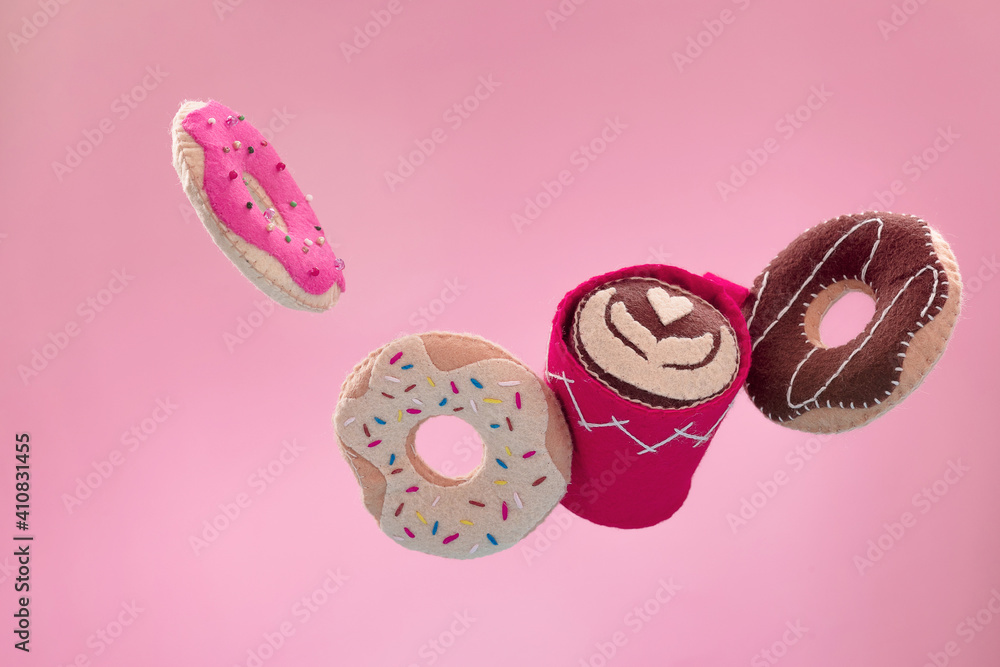 Handmade felt doughnuts flying in the air are on a pink background with a cup of cappuccino . Fake bakery, craft concept, diet joke right breakfast. Levitation