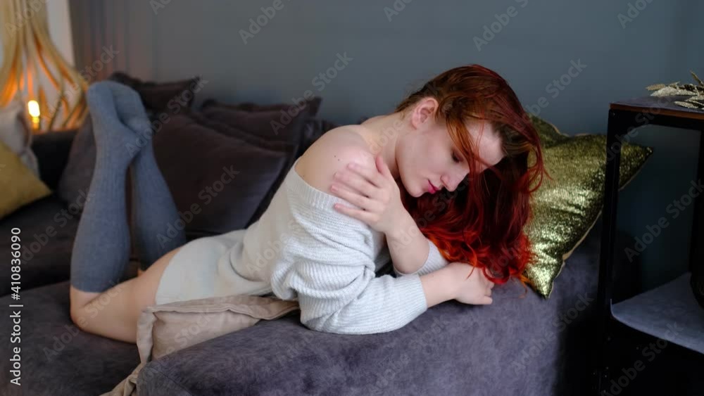 Attractive happy girl lying on her stomach on cozy sofa in harmony enjoying daydream in bright air fresh living room. time for rest and relaxation Attractive happy girl lying on her stomach on cozy sofa in harmony enjoying daydream in bright air fresh living room. time for rest and relaxation