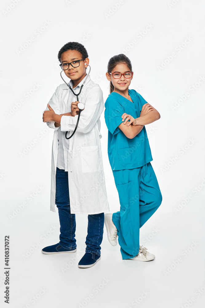 Cute kids wearing a medical uniform with arms crossed on white background. Two children play medical staff and choose a medical profession Cute kids wearing a medical uniform with arms crossed on white background. Two children play medical staff and choose a medical profession