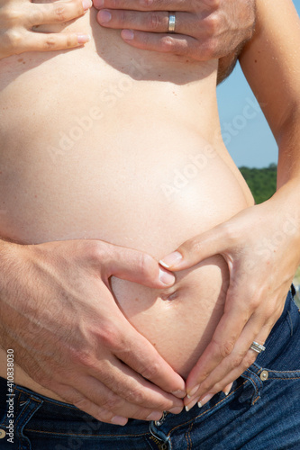 pregnant woman and man embracing naked topless abdomen belly with hands outdoor