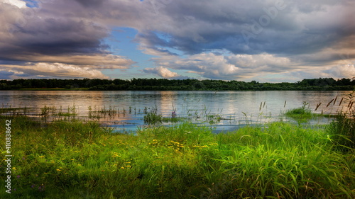 summer landscape with a river and storm clouds. before the rain. beautiful overgrown beach with grass and flowers