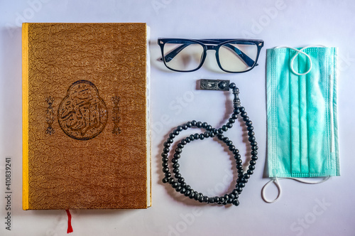 Holy Book of Quran with, rosary beads or tasbih, reading glasses and face mask on white background. Ramadan concept, Islamic religious ritual