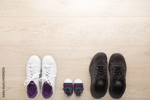 Father, mother and little kid sport shoes on wooden floor background. New family. Closeup. White female, black male and blue baby footwear. Empty place for text. Top down view.