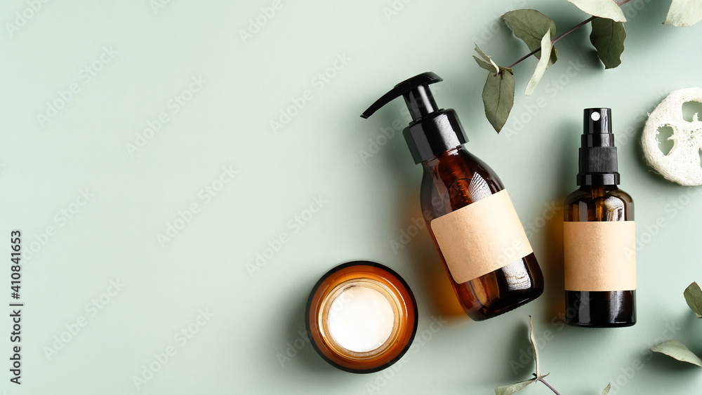 Natural organic SPA cosmetic products set with eucalyptus leaves. Top view herbal skincare beauty products on green background. Amber glass dispenser, spray bottles, jar of moisturizer cream. Natural organic SPA cosmetic products set with eucalyptus leaves. Top view herbal skincare beauty products on green background. Amber glass dispenser, spray bottles, jar of moisturizer cream.