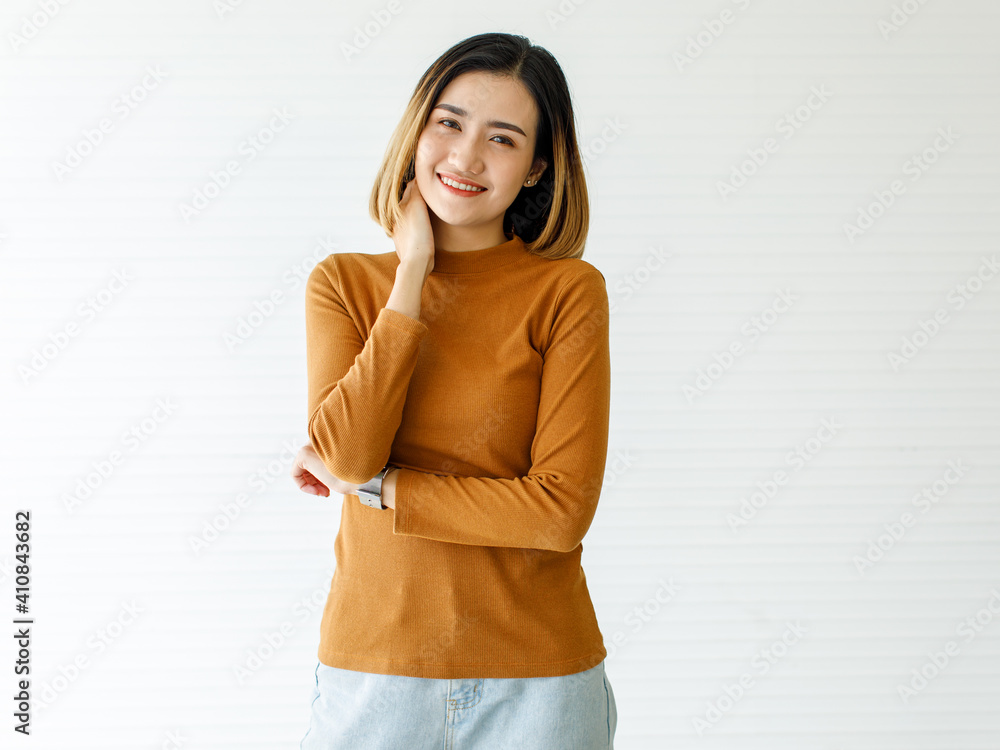 Vertical medium shot portrait of a cute smiling Asian woman with golden short straight hair in a casual long sleeve brown clothes and blue jeans posing in the studio isolated with white background Vertical medium shot portrait of a cute smiling Asian woman with golden short straight hair in a casual long sleeve brown clothes and blue jeans posing in the studio isolated with white background