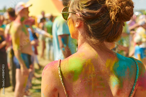 the graceful back of a girl in round glasses, stained with paints at the festival of holi colors against the backdrop of a cheerful colored crowd photo