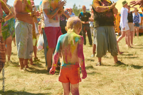 a child in a crowd stained with beautiful colorful paints at the holi festival of colors, view from the back