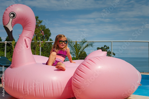 cute baby girl sitting over huge pink inflatable flamingo