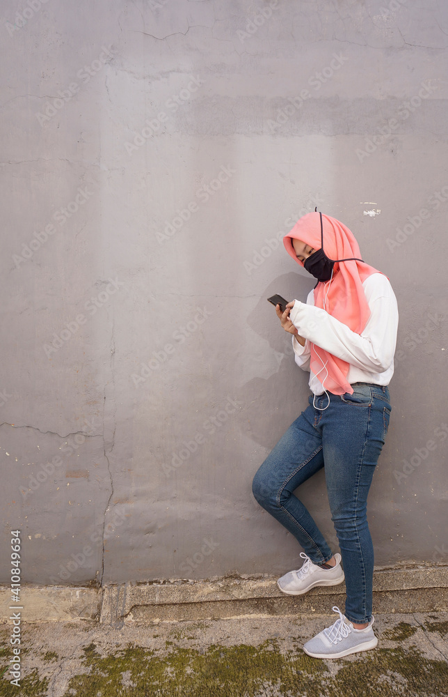 Muslim asian girl wearing face mask due to corona virus pandemic looking to her phone