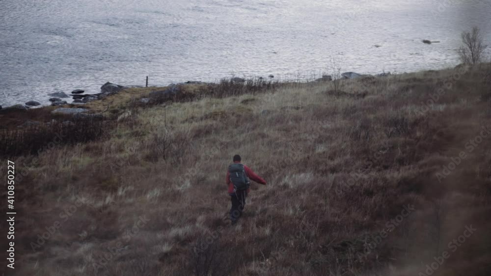 Hiker Walking In Grass Towards Fjord Hiker Walking In Grass Towards Fjord
