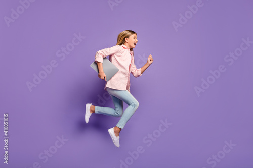 Full size profile photo of optimistic pretty girl jump run wear pink shirt jeans sneakers hold laptop isolated on violet background