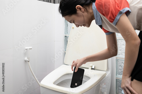Unhappy asian child girl crying picking up mobile phone that fell in water,sad people holding smartphone wet after falling it,drop into toilet bowl in bathroom,regret the careless handling of phone.