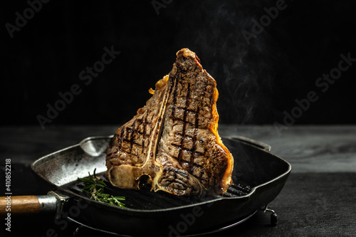 Grilling a tasty tender marinated t-bone steak seasoned with fresh rosemary on frying grill pan on black. wagyu porterhouse grilled beef steak. banner, menu, recipe, place for text photo