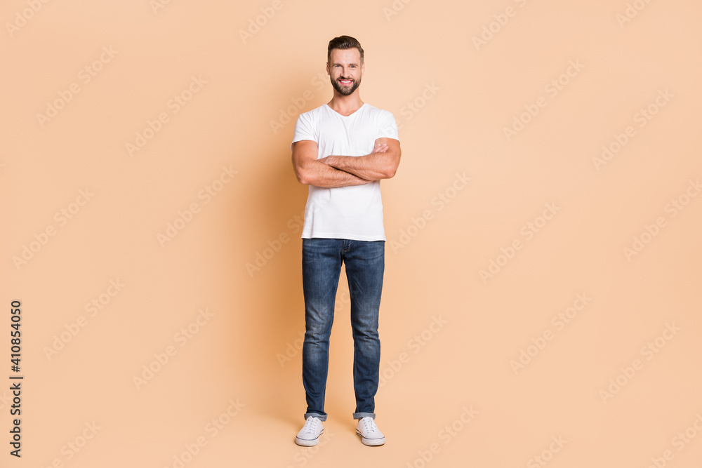Full length photo of young handsome man happy positive smile confident crossed hands isolated over beige color background Full length photo of young handsome man happy positive smile confident crossed hands isolated over beige color background