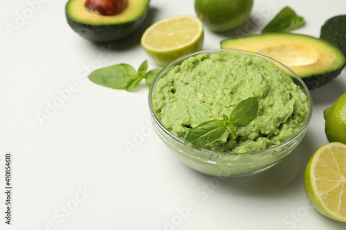 Bowl of guacamole, avocado, lime and basil on white background, space for text