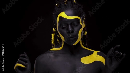 Face art. Dancing woman with black and yellow body paint. Young african girl with colorful bodypaint. An amazing afro american model with yellow makeup. Closeup face. photo