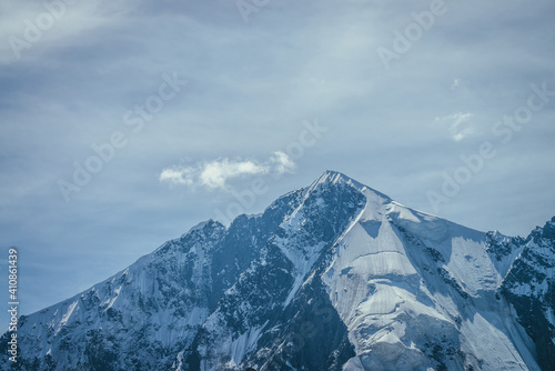 Awesome mountains landscape with big snowy mountain pinnacle in blue white colors and white cirrus clouds in blue sky. Atmospheric highland scenery with high mountain wall with pointed top with snow.